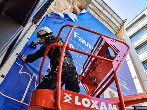 homme qui accroche une bâche de chantier sur un immeuble