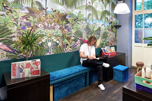 un homme qui lit un livre devant une tapisserie végétale