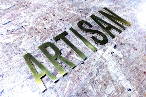 Un lettrage découpé en laiton écrit ARTISAN